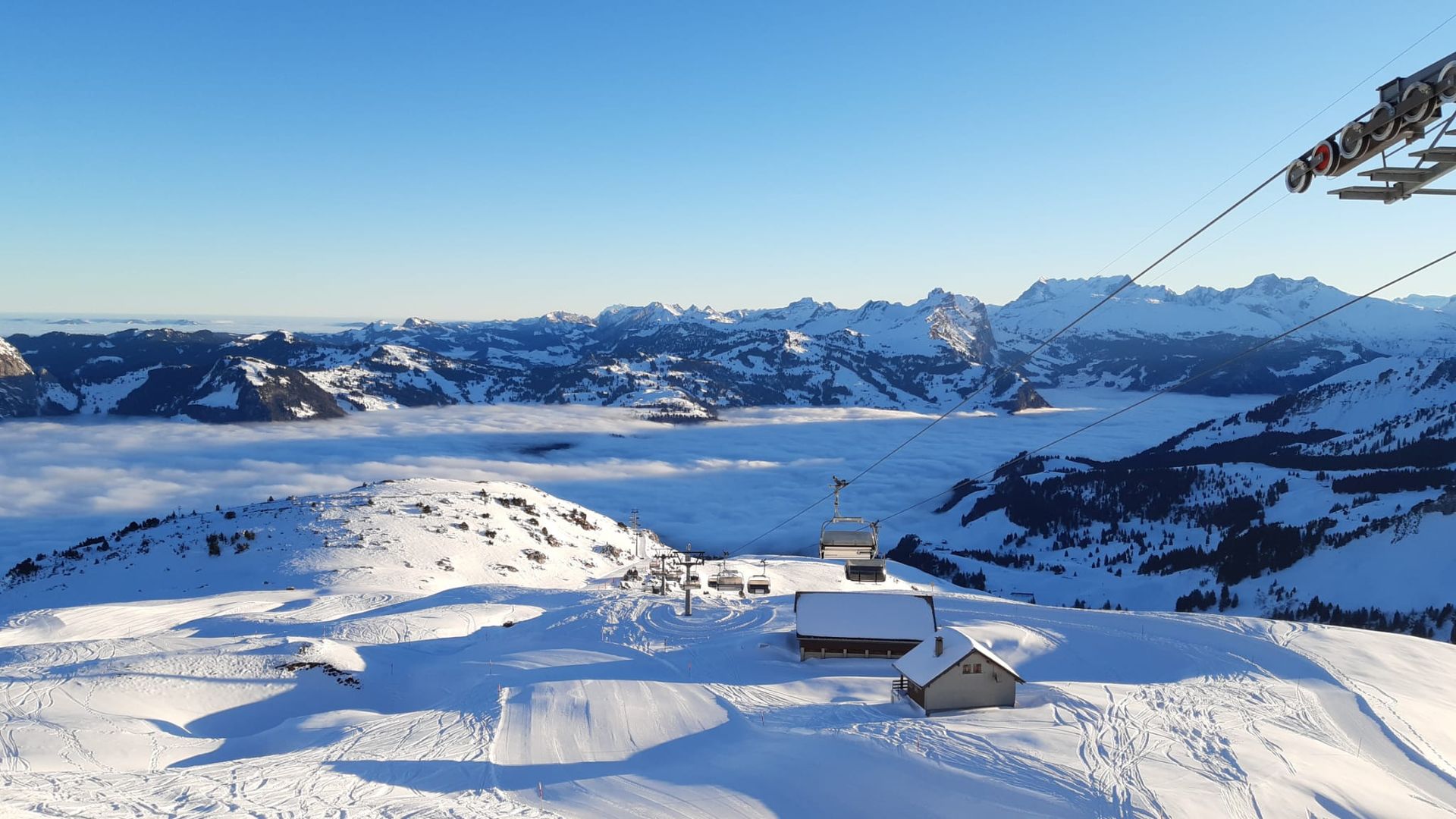 A bustling winter sports scene at Stoos-Fronalpstock | Klingenstock ski resort in Central Switzerland. A mountain hut nestles amidst beautiful winter scenery complete with snow covered slopes and peaks.