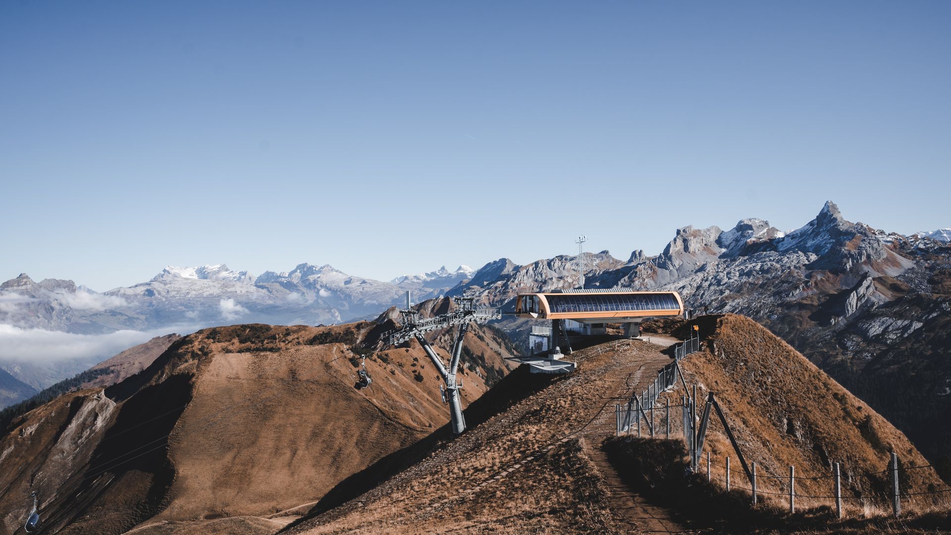 A scenic view of the Stoos - Fronalpstock | Klingenstock ski resort in Schwyz Switzerland. Features a ski lift traversing up a mountain a mountain bike parked nearby and a quaint chalet nestled into the landscape.