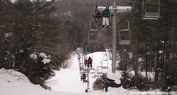 Winter sports scene at Lost Valley, None, Maine, featuring a ski lift ascending a snow-covered slope amidst a stunning winter panorama. A quaint chalet is nestled amidst the snowy landscape.