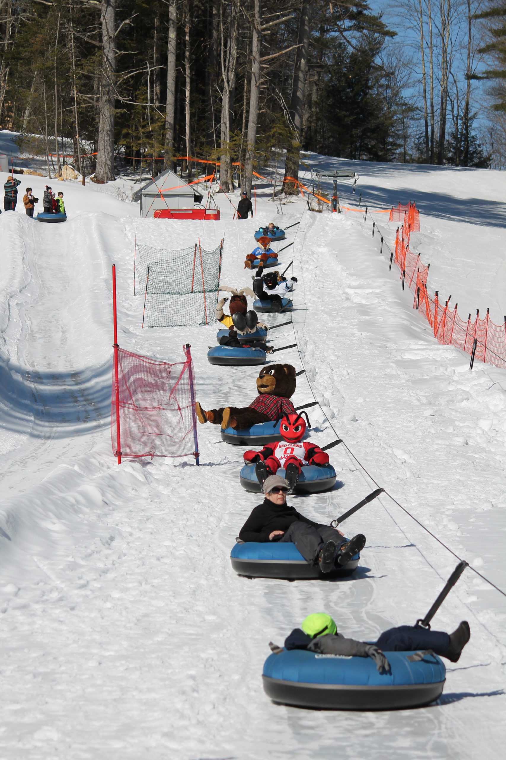 A vibrant winter sports scene at Lost Valley Maine featuring happily active skiers and snowboarders. A ski lift operates in the background surrounded by a picturesque snow-covered resort.