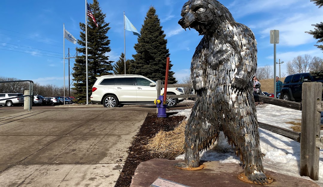A skier and a snowboarder at Great Bear Ski Valley, South Dakota, enjoying winter sports. A cozy challet and a ski resort serve as a backdrop amidst a serene, snowy landscape.