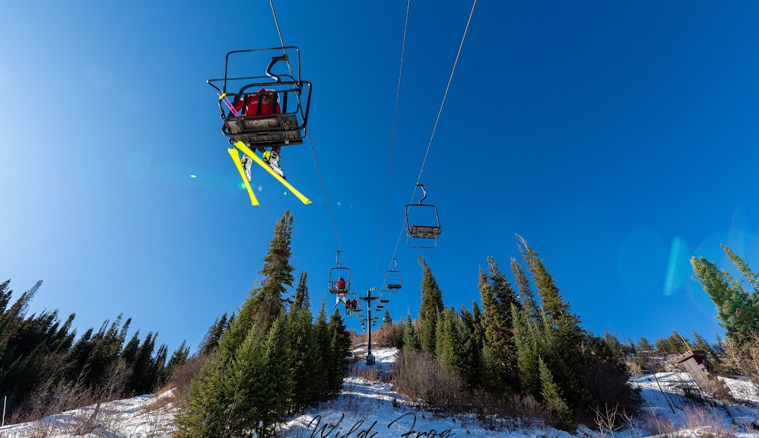 A picturesque wintry scene at Howelsen Hill Steamboat Springs Colorado USA. A ski lift carries eager skiers up the slopes amidst a lively landscape of winter sports. Ski resort infrastructure and a snowmobile are also visible.