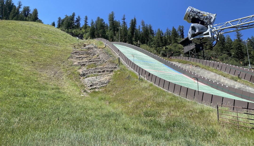 A scenic view of Howelsen Hill in Steamboat Springs Colorado displaying a ski lift and resort. A mountain bike and a challet are seen with a skier dotting the crisp snowy slopes.
