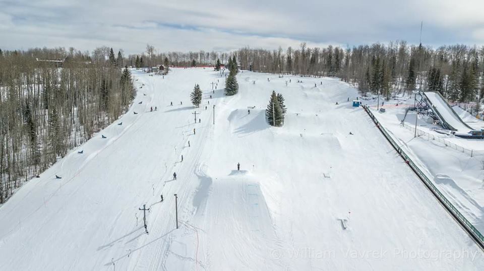 Winter sports scene at Nitehawk, Northern Alberta, Canada, featuring a ski resort with a skier on the slopes and a ski lift in the background.