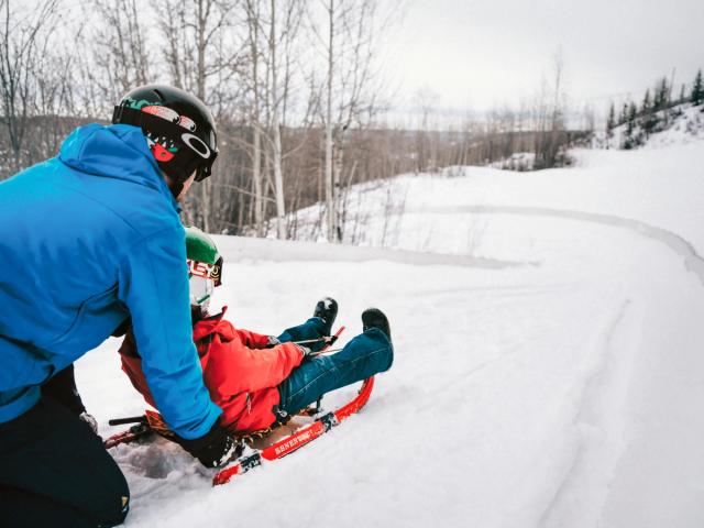 A snowboarder is mid-action on the slopes at Nitehawk, Northern Alberta, Canada. The white snow provides a sharp contrast to the gear, illustrating a thrilling winter sports scene.