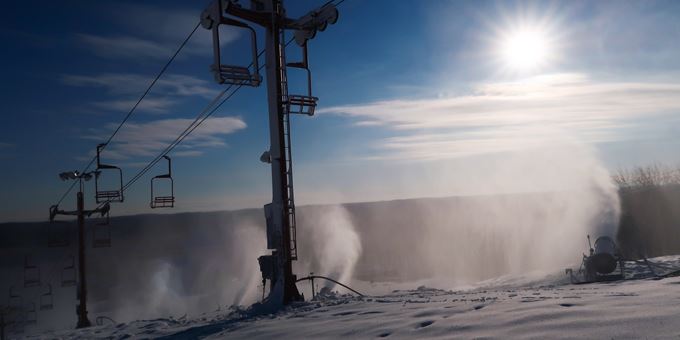 Winter scene at Sunburst in Wisconsin, USA showcasing a ski lift ascending towards a quaint challet, with various sports activities happening in the foreground at this popular ski resort.