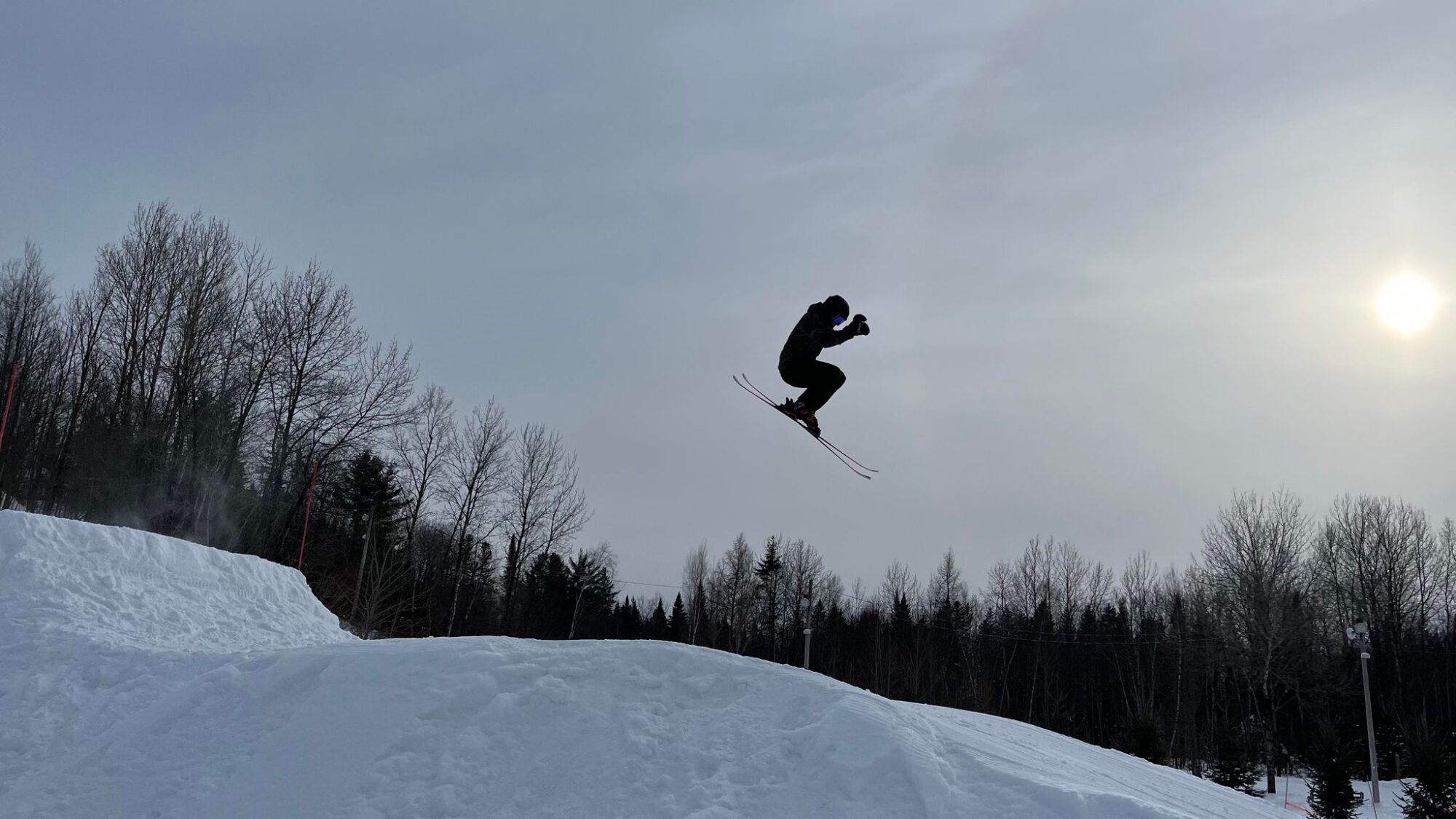 A skier and snowboarder enjoy a winter sports scene in Saint-Raymond Quebec perhaps nearing a chalet and snowmobile in the distance.