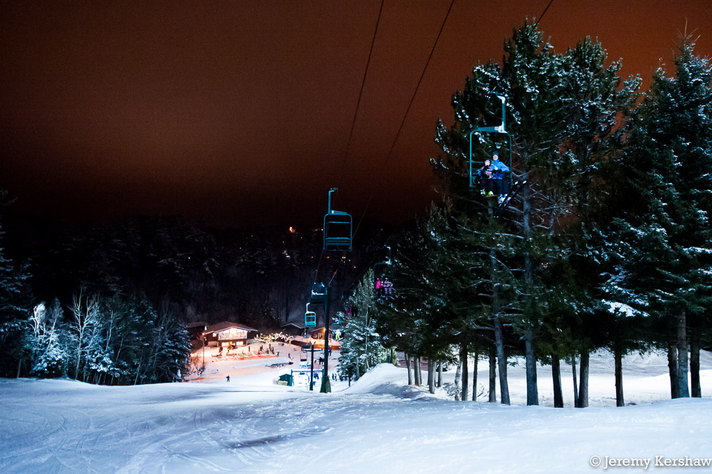 Winter scene at Chester Bowl, Minnesota, featuring a ski lift operating amidst snow-filled surroundings, with a skier and snowboarder in action at the ski resort.
