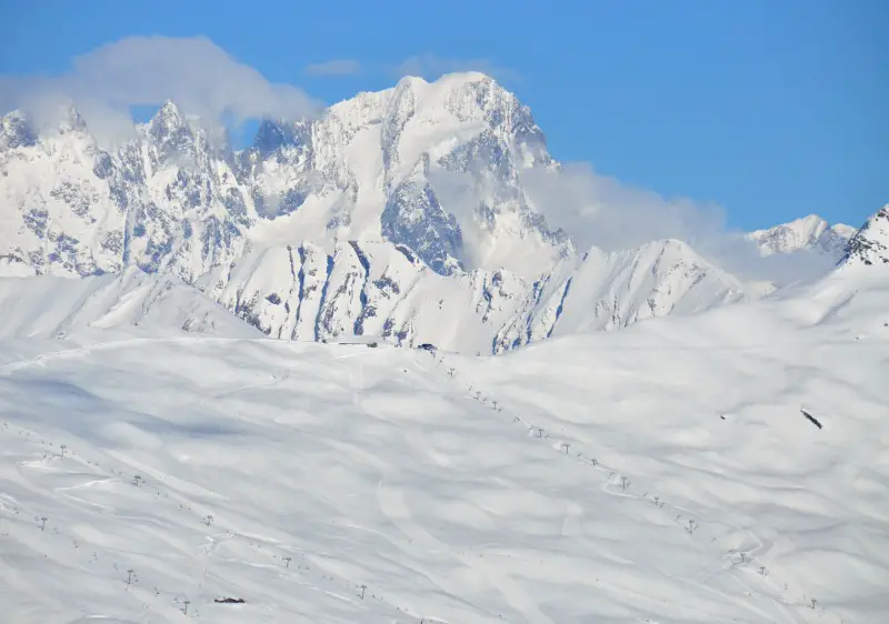 View of the beautiful Espace San Bernardo - La Rosière in France, featuring a skier gliding down a snowy mountain slope, with a charming chalet and extensive ski resort in the backdrop.