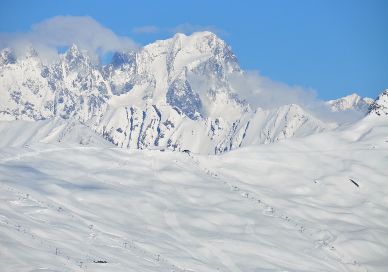 View of the beautiful Espace San Bernardo - La Rosière in France, featuring a skier gliding down a snowy mountain slope, with a charming chalet and extensive ski resort in the backdrop.