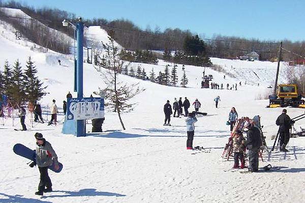Winter sports enthusiasts enjoy the snowy slopes at the Holiday Mountain ski resort in Manitoba, Canada, with a charming chalet and ski lift visible nearby.