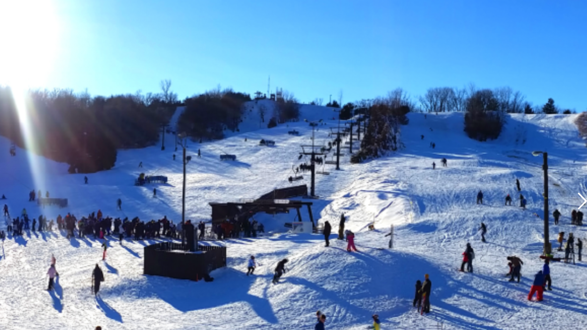 Winter scene at Mt Crescent, Iowa, featuring a bustling ski resort and winter sports center amid a breathtaking snowy landscape, with a chalet partially visible.