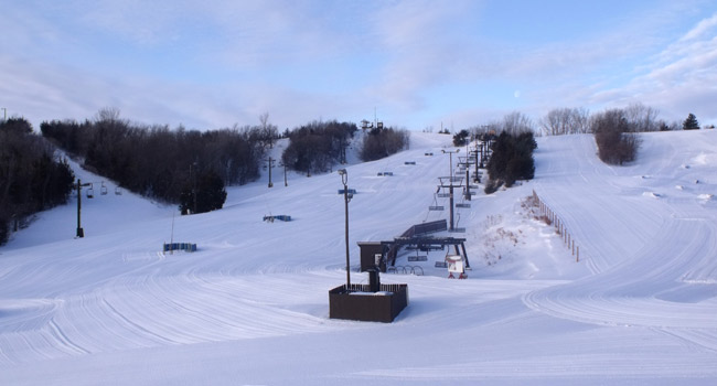 A winter scene at Mt Crescent Iowa showcasing a ski resort with a ski lift operating amongst snow-covered slopes implying a bustling winter sports activity.