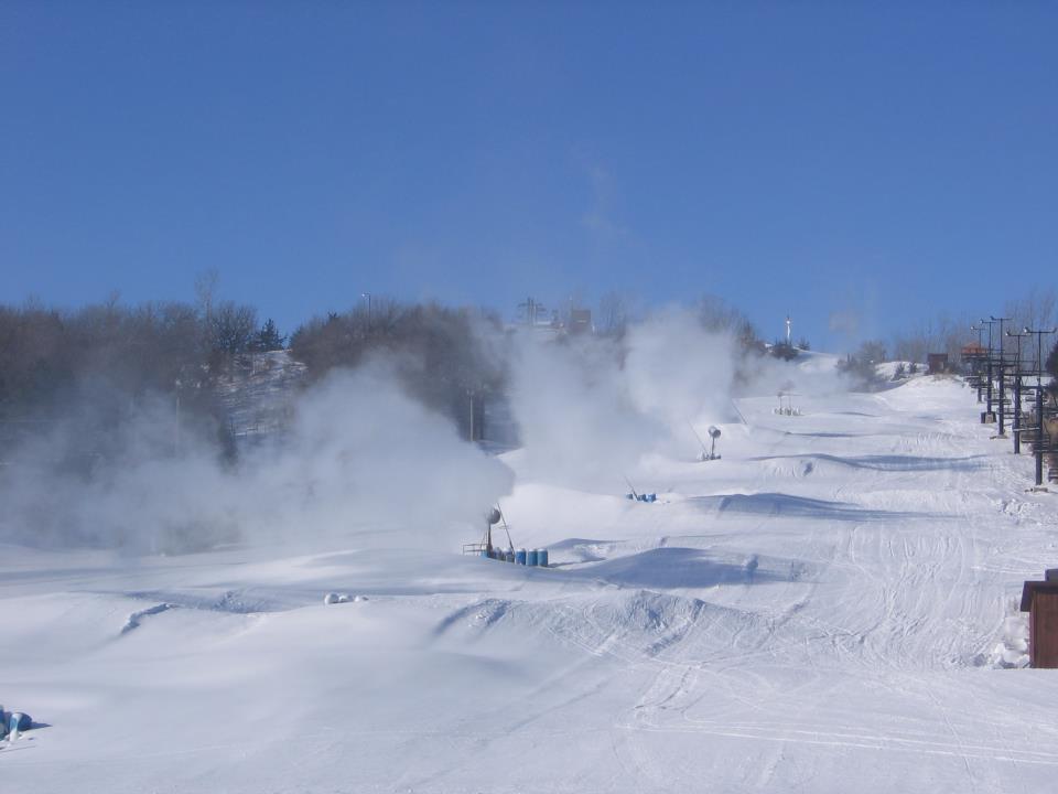A view of the bustling Mt Crescent ski resort, Iowa, covered in beautiful white snow. Winter sports enthusiasts can be seen skiing down the slopes and utilizing the ski lift onsite.