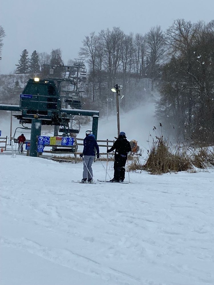 A winter sports enthusiast skiing down a slope at Uplands Ski Centre in Southern Ontario Canada with a ski lift and resort in the backdrop.