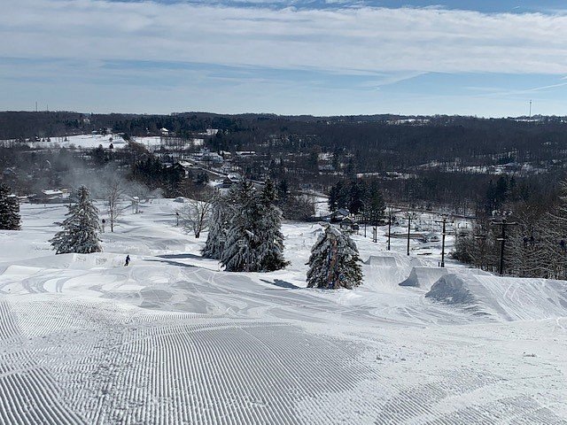 Winter scene at Alpine Valley, Ohio, portraying a bustling ski resort with people enjoying winter sports on snow-covered slopes, with ski lifts and a chalet in the background.