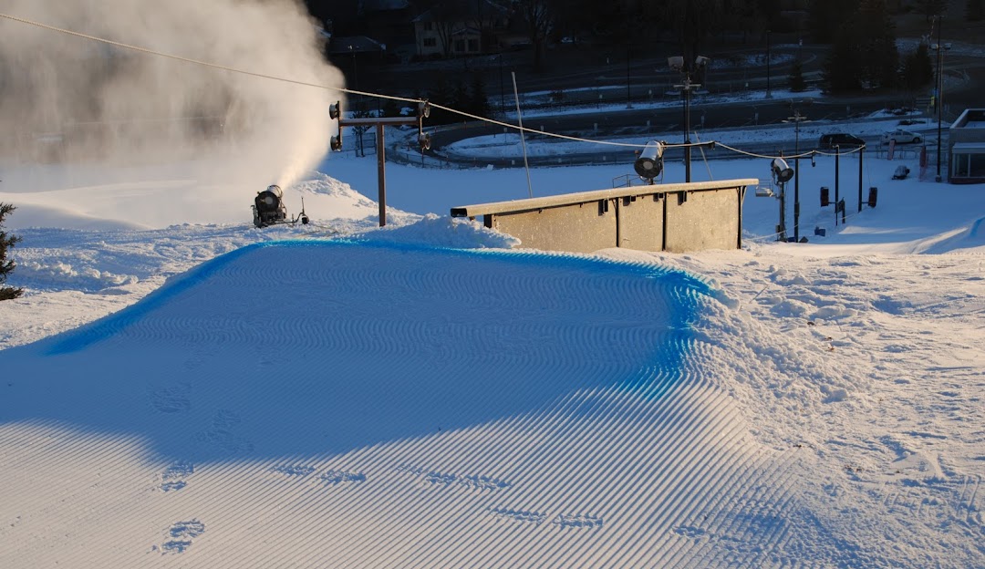 A bustling winter scene at Hyland Hills Minnesota showcasing a vibrant winter sports centre and a ski resort. Skiers glide down the snow-covered hills amidst presence of snowmobile.