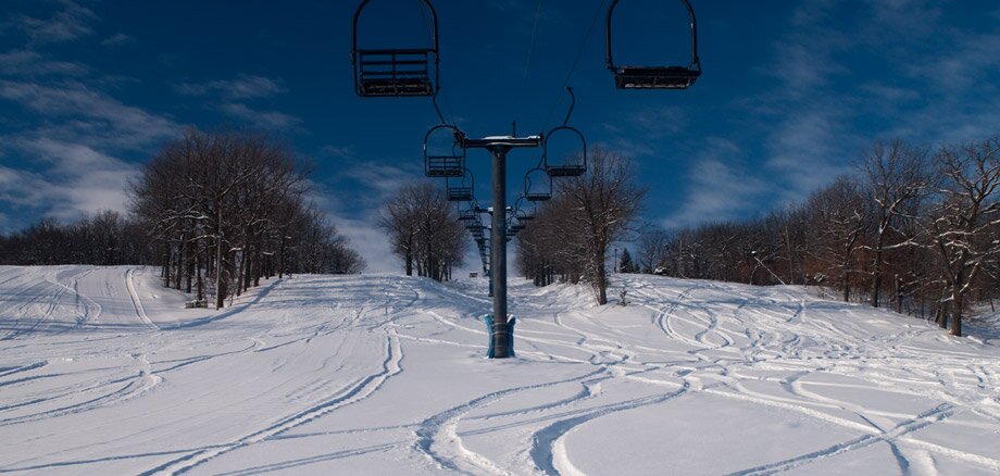 Ski lift ascending Bear's Den Mountain in Fort Ransom, North Dakota amidst a winter landscape. Skiers enjoy the snowy terrain near a cozy chalet at this ski resort.