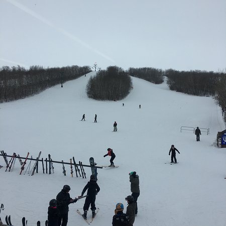 A picturesque scene at Minnedosa Ski Valley Manitoba featuring a chalet ski resort and action-packed winter sports scene. Skiers are seen enjoying the slopes with a ski lift nearby.