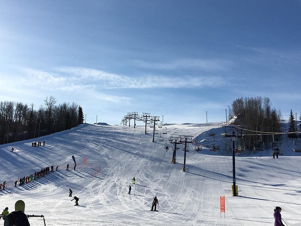 Winter scene at Rabbit Hill Snow Resort in Edmonton Alberta with skiers and snowboarders on the slopes the ski lift in operation and a chalet nestled in the snowy landscape.