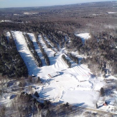 An enchanting winter scene at Hermon Mountain in Maine, featuring a bustling ski resort dotted with chalets, amidst the breathtaking beauty of the white, snowy landscape.