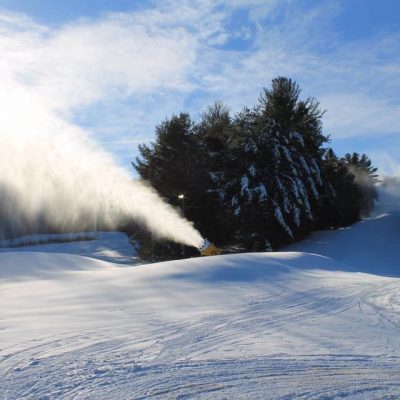 Winter sports enthusiasts enjoying a day at Hermon Mountain Ski Resort in Maine, USA. Stunning winter scene with skiers and a snowmobile spotted amidst the snowy landscape.