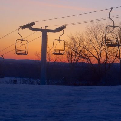A ski lift ascending Hermon Mountain in Maine USA in a winter sports scene. Skiers enjoy the ski resort amongst the stunning winter scenery with snow blanketing the landscape.