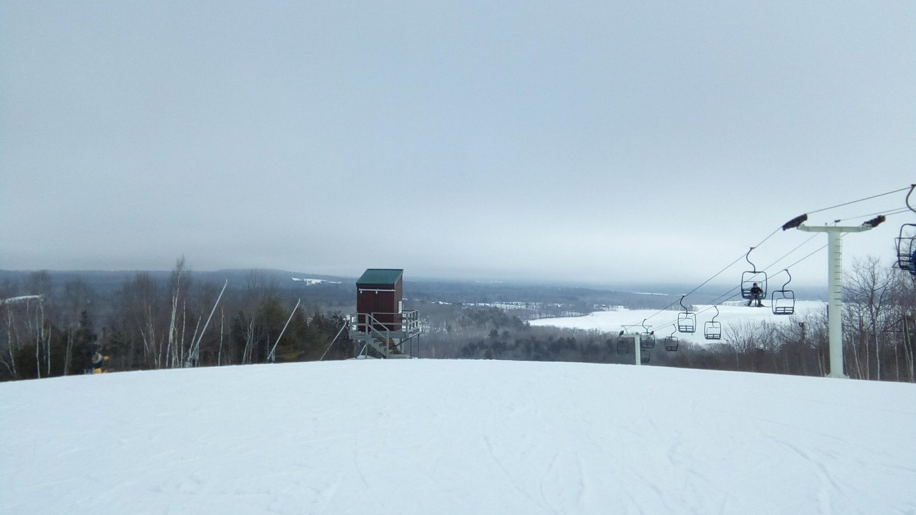 Winter scene at Hermon Mountain in Maine, USA featuring a snow-covered ski resort with a skier in action and a ski lift in the backdrop amidst the charming winter landscape.