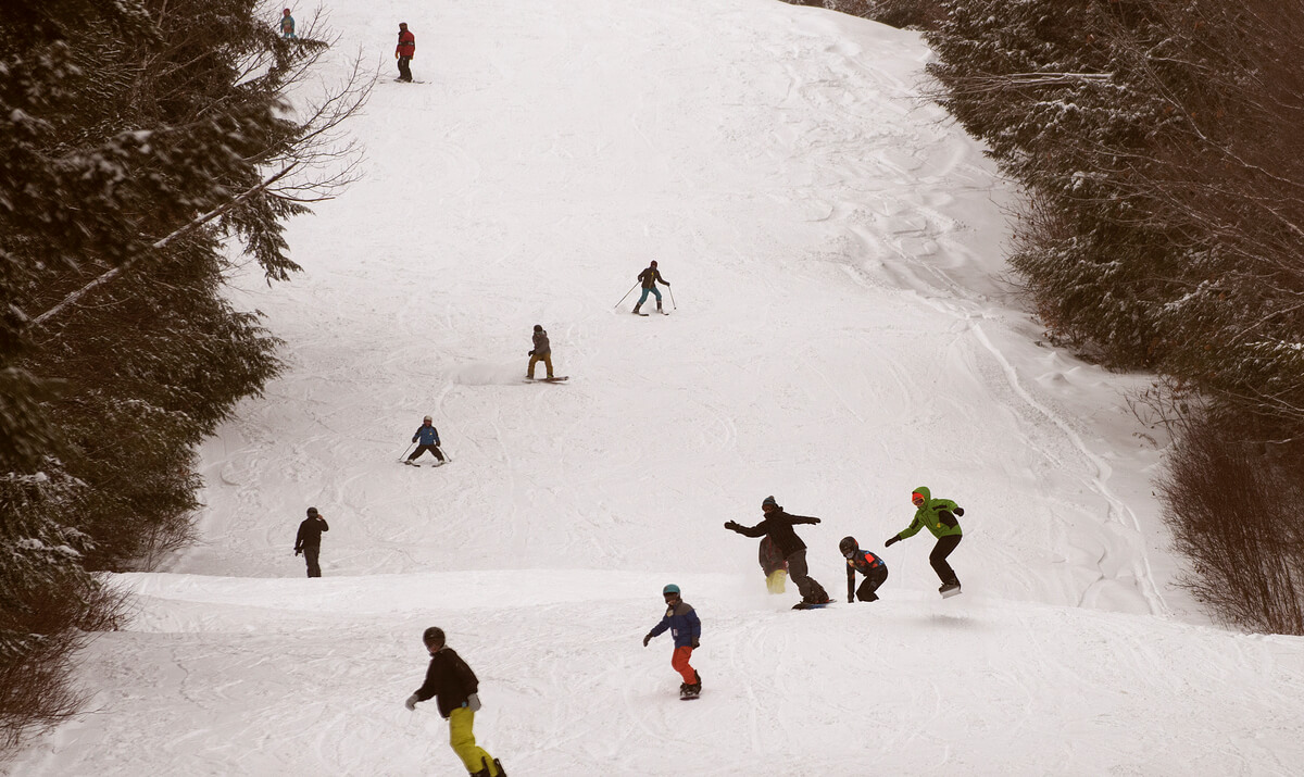 A bustling winter sports scene at Hermon Mountain Maine featuring a skier and group of people skiing at the ski resort complete with a cozy challet.