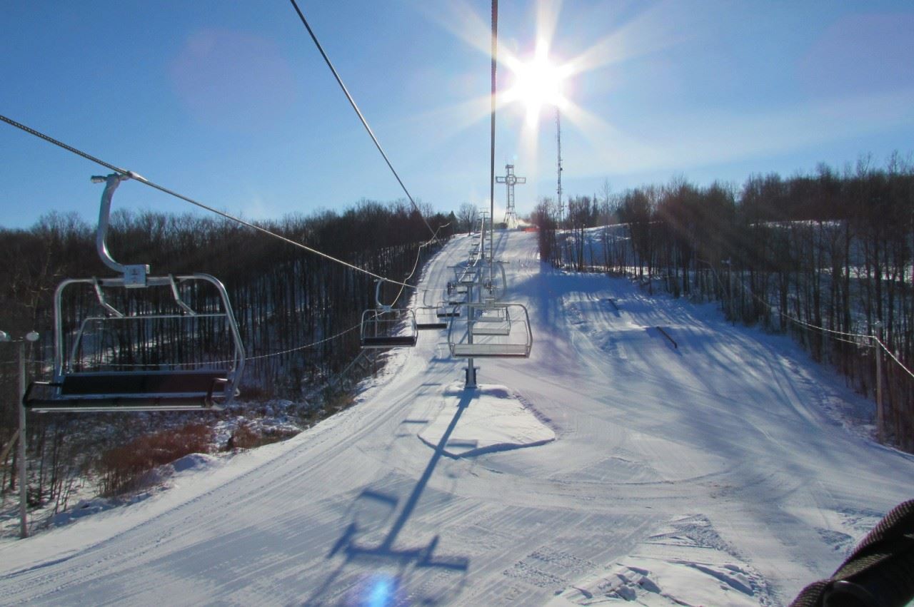 A winter sports scene at Mont Bellevue Quebec showing a ski lift and skier amidst the charm of a bustling ski resort and sports centre.