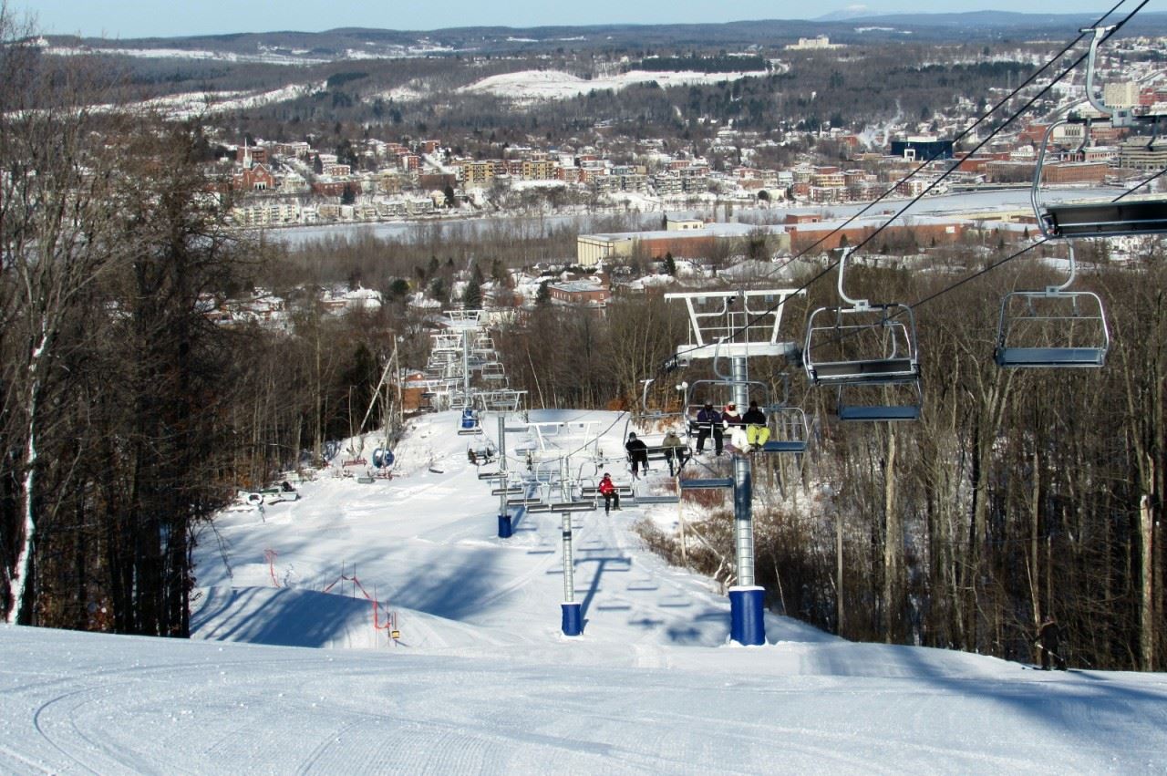 Ski resort scene at Mont Bellevue, Quebec, showcasing a ski lift ascending the snowy hill, a quaint chalet nestled nearby, and a skier enjoying the winter sports activities.