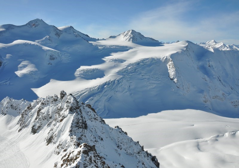 View of the majestic Pitztal Glacier in Tyrol, Austria featuring snowy peaks, a mountain chalet, and bustling ski resort surrounded by pristine, snow-covered slopes.
