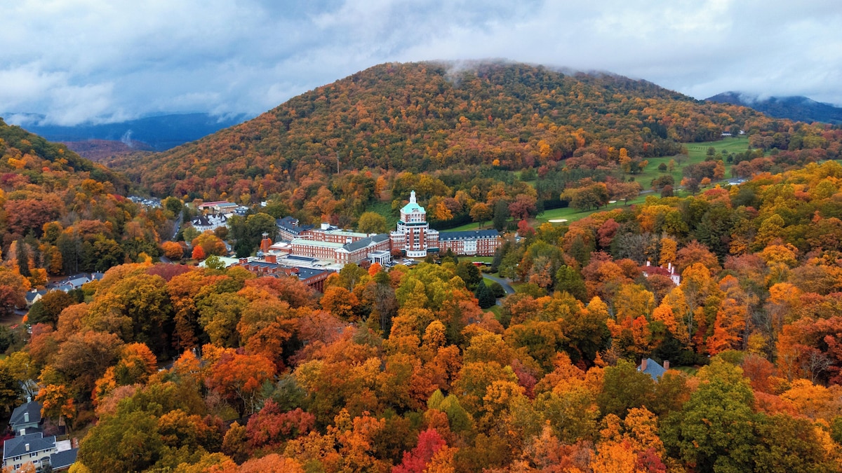 A picturesque view of The Omni Homestead in Virginia featuring a majestic mountain backdrop a charming ski resort chalet and an engaging winter sports scene surrounded by stunning winter scenery.