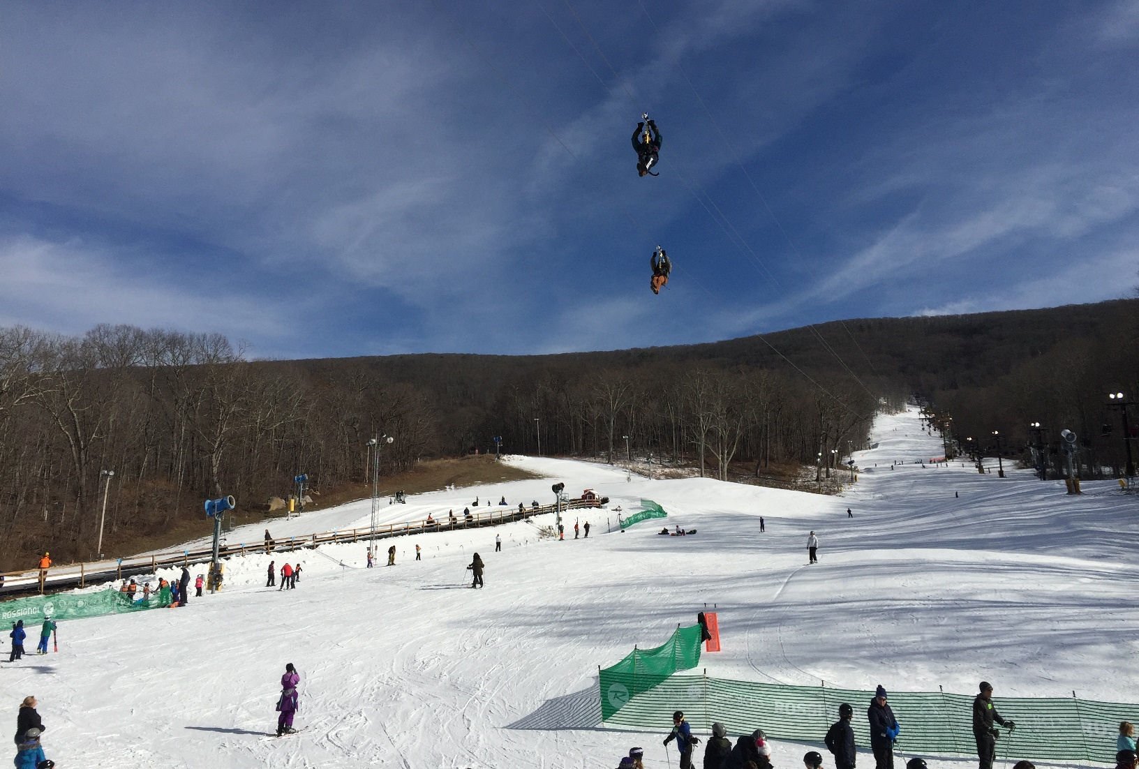 A scenic image of The Omni Homestead in Virginia highlighting a winter sports scene featuring a skier and a snowboarder amidst a snow-filled ski resort with a visible ski lift.
