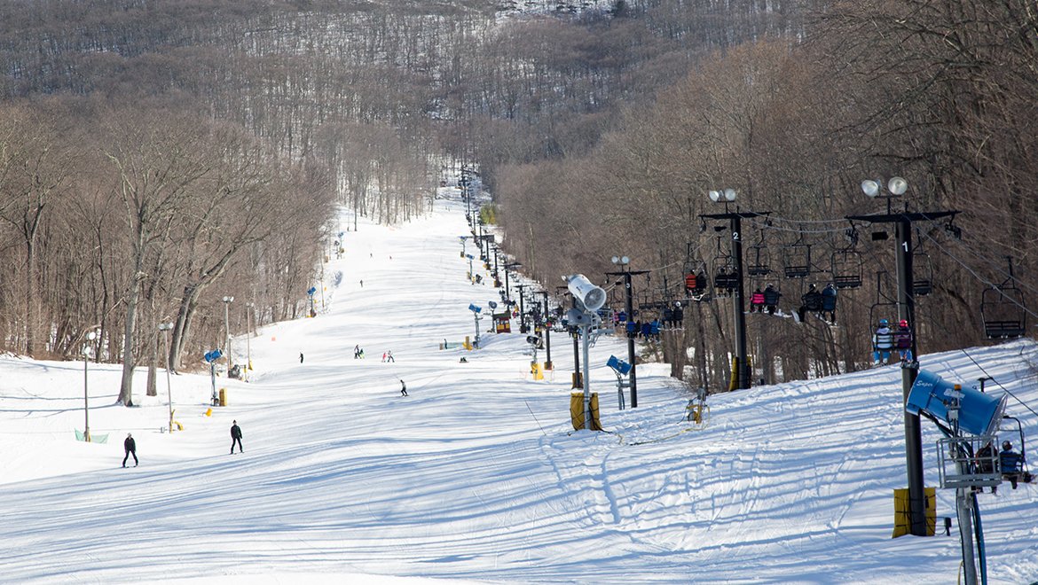 Winter sports scene at The Omni Homestead in Virginia, USA, featuring a bustling ski resort, skiers traversing snowy slopes, a functioning ski lift, amidst stunning winter scenery.
