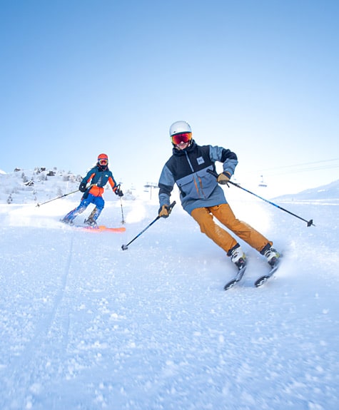 Winter sports scene in Val Cenis, France, featuring a skier swooshing down the snowy slope. A winter sports center and a cozy chalet are visible in the backdrop, alongside a group of fellow skiers.