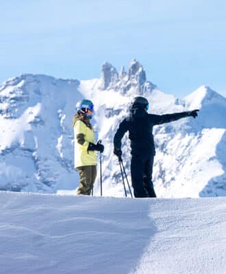 Winter scene at Val Cenis ski resort in France showing a skier gliding past a charming chalet, with other family members skiing in the background.