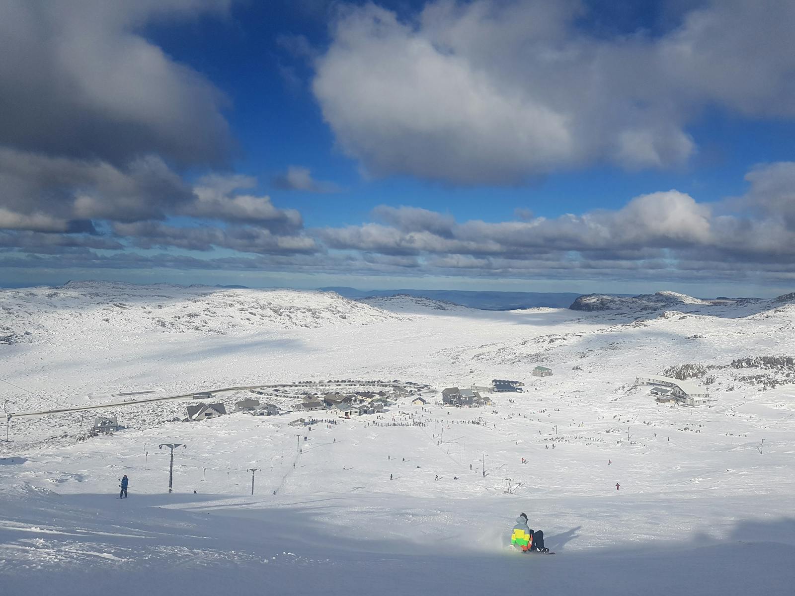 A scene from Ben Lomond Tasmania showing a chalet amidst a bustling winter sports scene. Ski resort features skiers skillfully maneuvering snowy slopes under a serene winter sky.