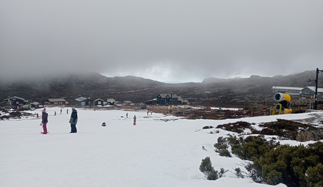 A winter sports scene at Ben Lomond in Tasmania, Australia, featuring a bustling ski resort amid stunning snow-covered scenery, with a skier making their way down the slopes.