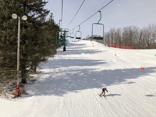 Skier descending a slope at Heiliger Huegel – Hubertus in Wisconsin, USA, with a ski lift and chalet visible in the winter sports resort scene.