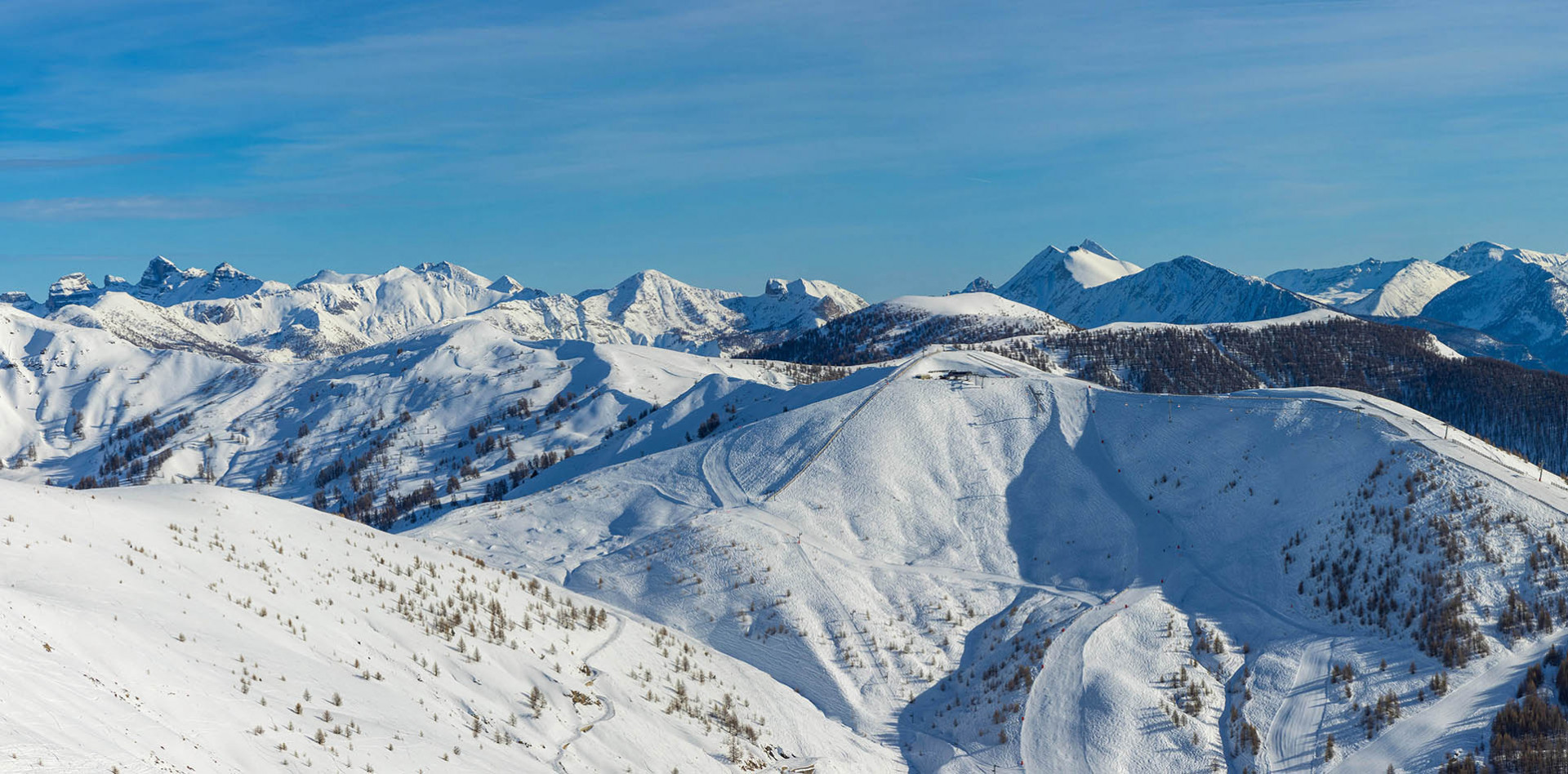 Ski resort scenery at Val d'Allos - Espace Lumière in France, featuring winter sports enthusiasts, a chalet, and vast snow-covered slopes against the backdrop of a majestic mountain.