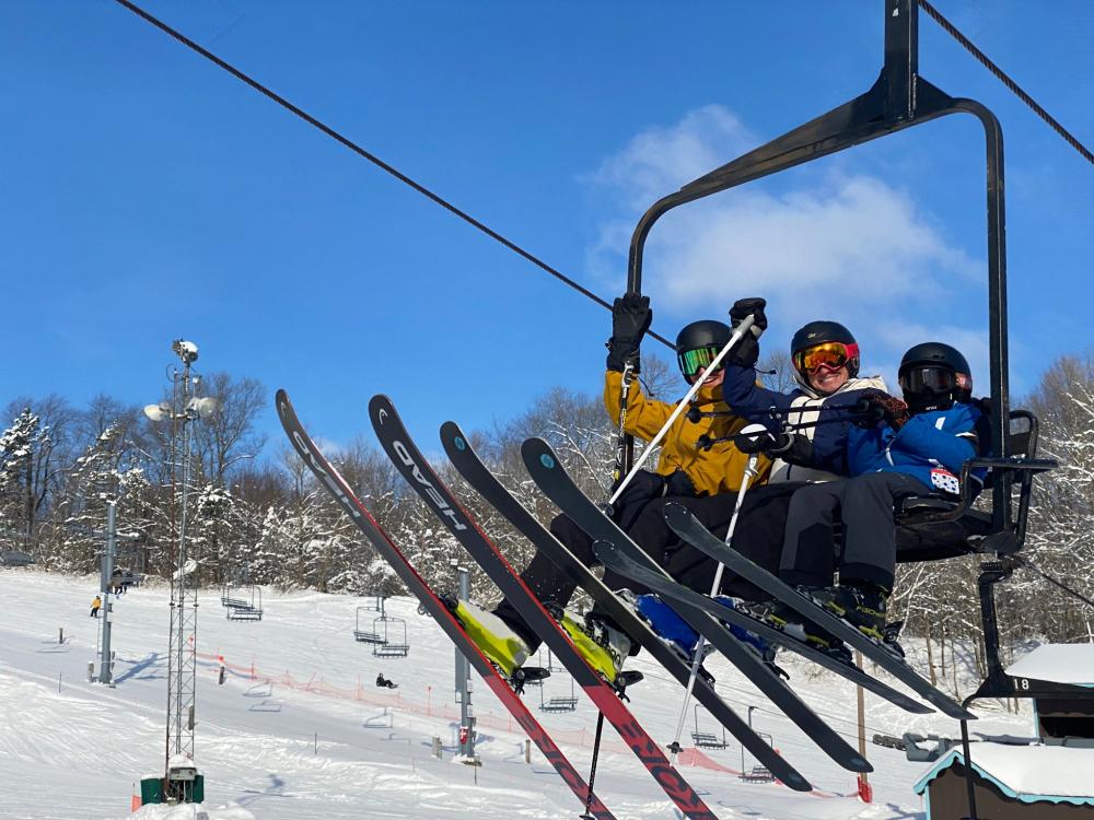 A winter sports scene at Swiss Valley, Michigan, showcasing a ski lift and groups of people, including families, enjoying their skiing time at the resort.