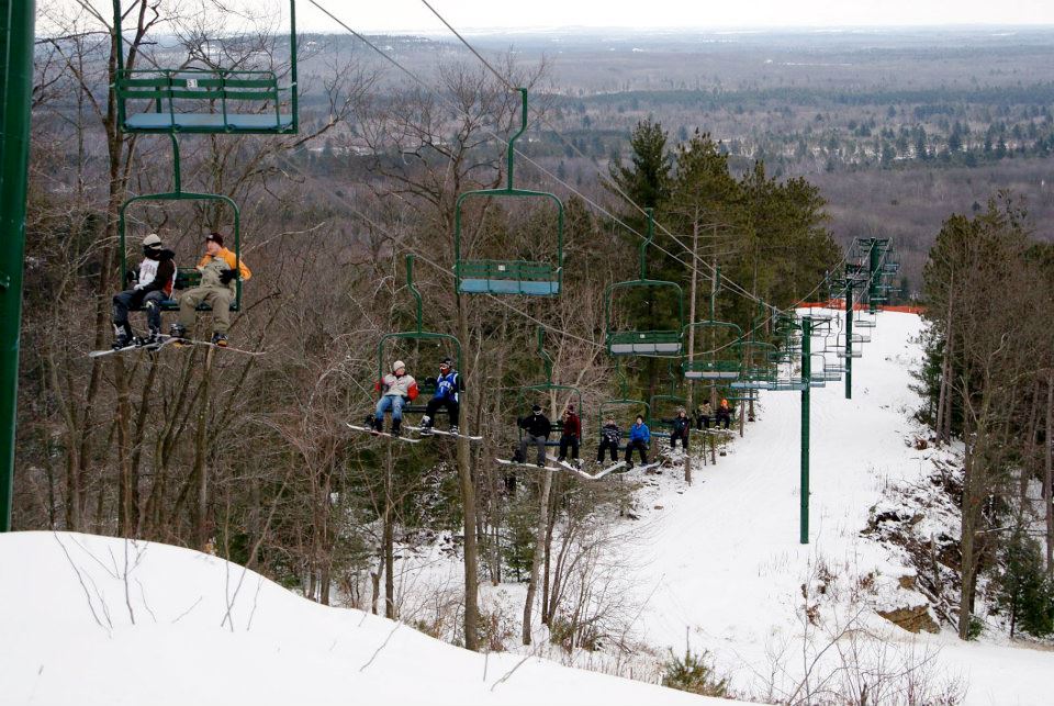 Skiers enjoying a beautiful winter's day at Bruce Mound in Wisconsin USA. They are scattered across the slopes and a ski lift can be seen indicative of a bustling ski resort.