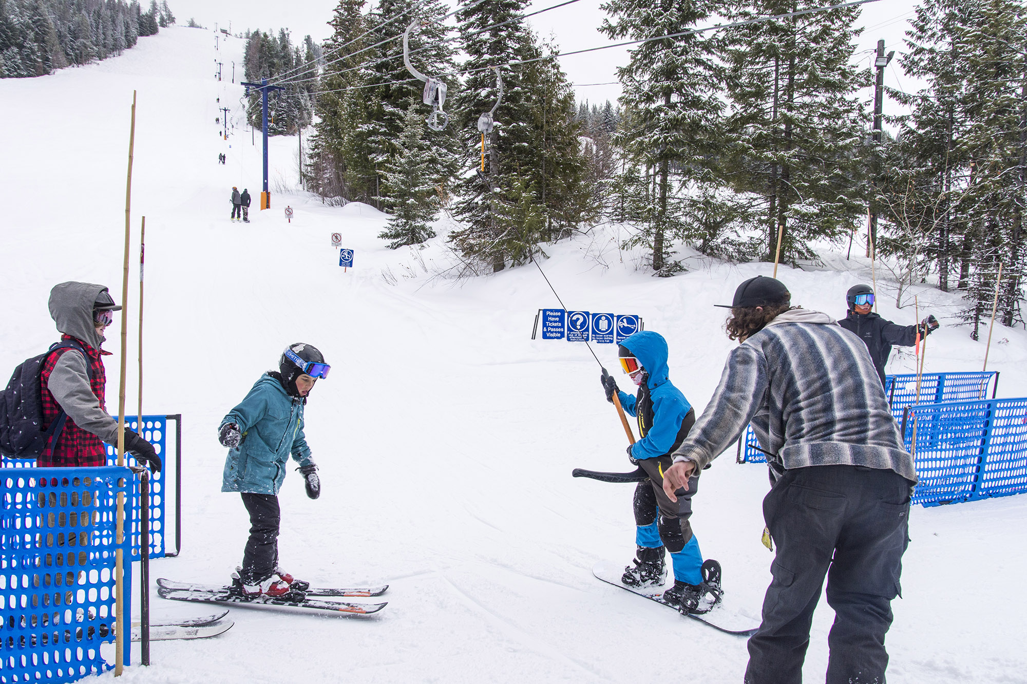 A family enjoying a day of skiing on the snowy slopes of Phoenix Mountain in British Columbia's Kootenay Rockies with a ski lift and resort in the background.
