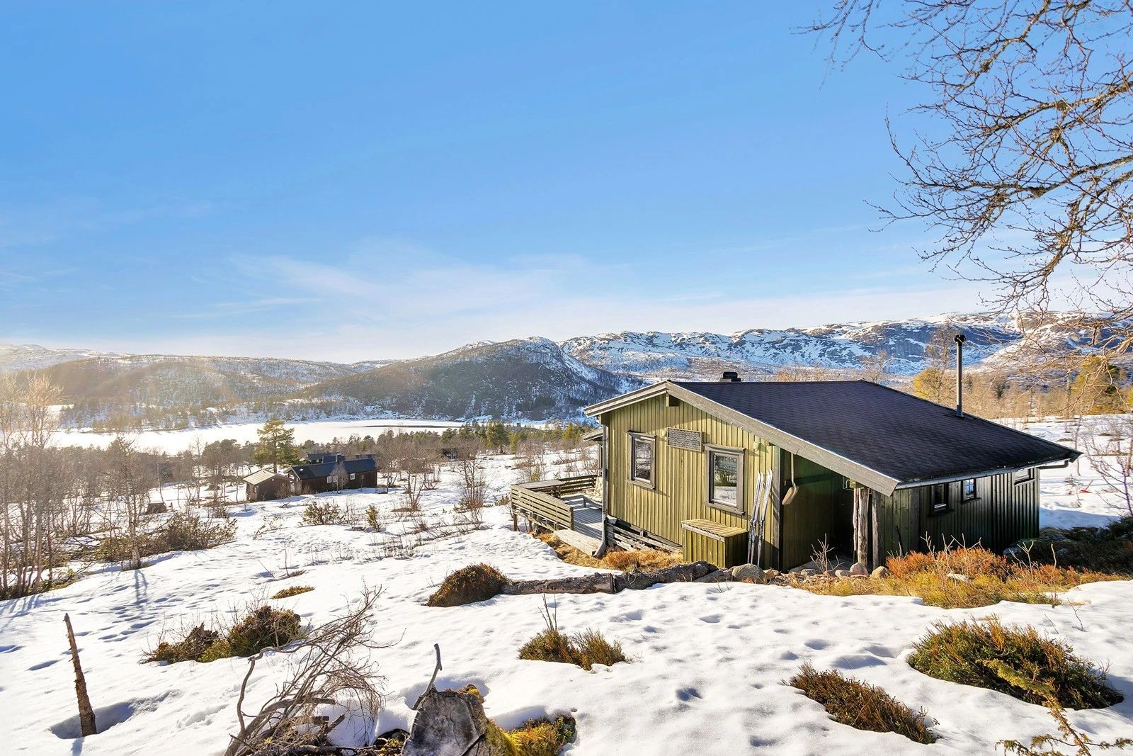 Hallbjønn in Norway - a green cabin in the snow with mountains behind.