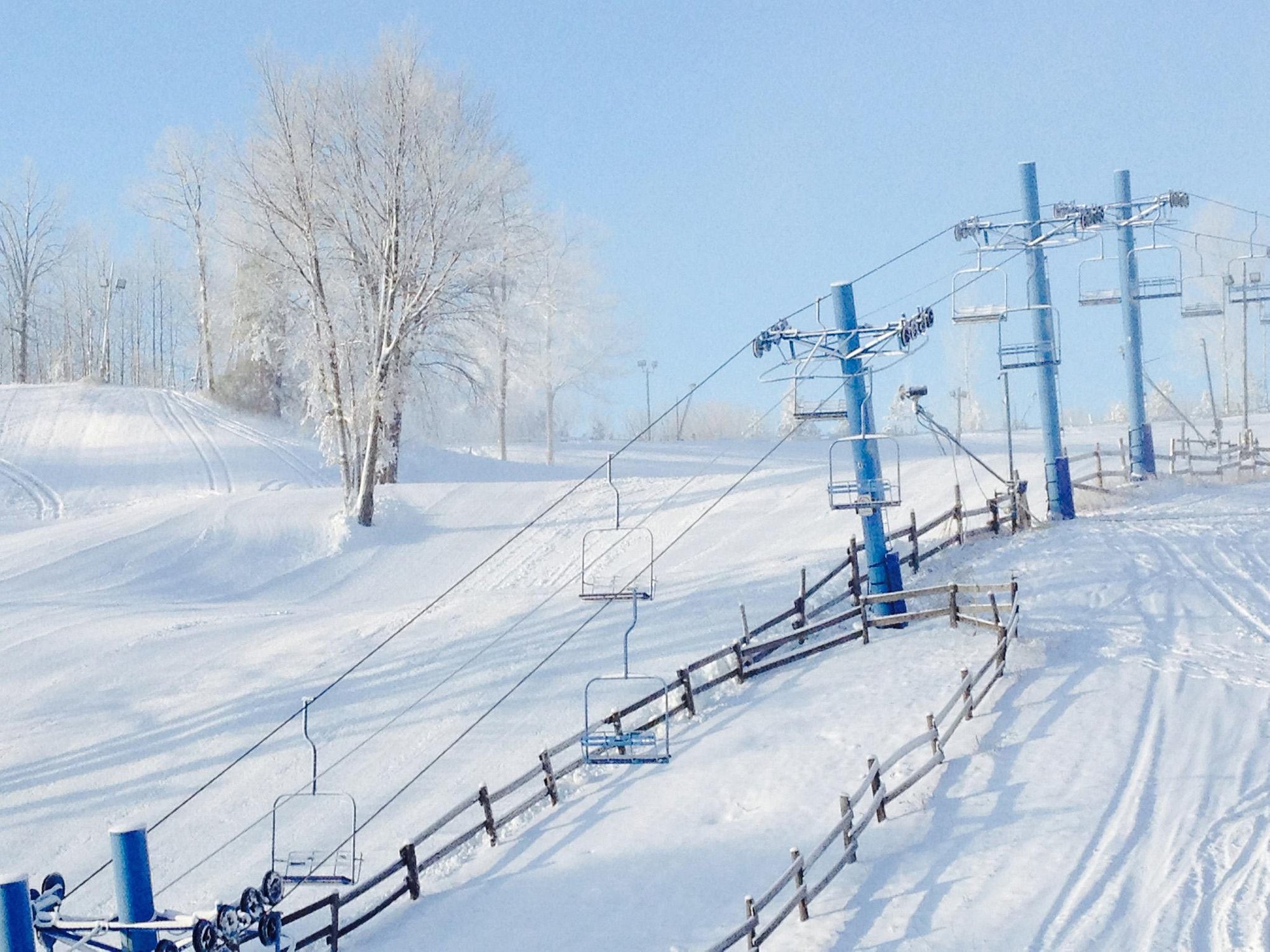 Winter sports enthusiasts enjoying a day at Snow Snake Ski Resort in Michigan, USA. A ski lift ascends the snowy, tree-lined slopes against a stunning winter landscape.