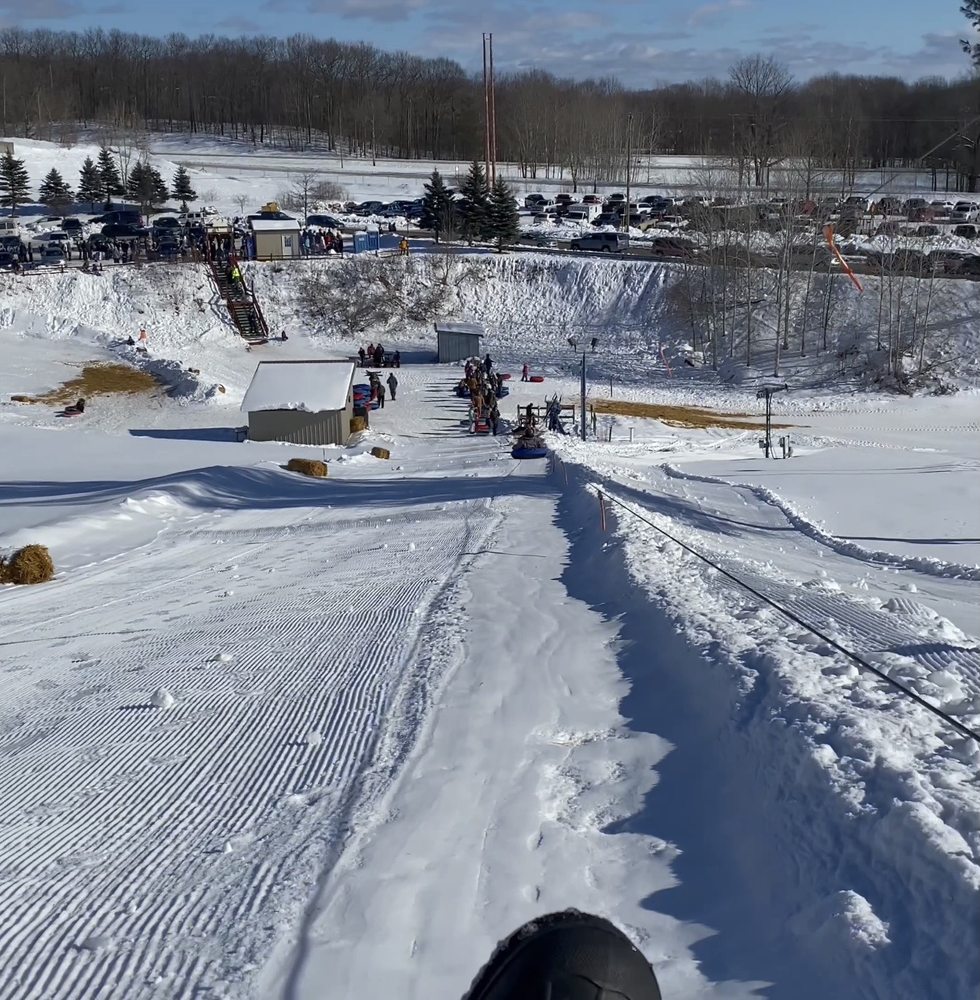 A lively winter sports scene at Snow Snake Ski Resort Michigan featuring a ski lift a skier and the nearby sports center blanketed under a thick layer of white snow.