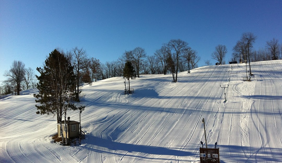 Winter sports scene at Snow Snake ski resort in Michigan, USA. Visible ski lift servicing the snowy slopes, with a picturesque chalet nestled nearby amidst stunning winter scenery.