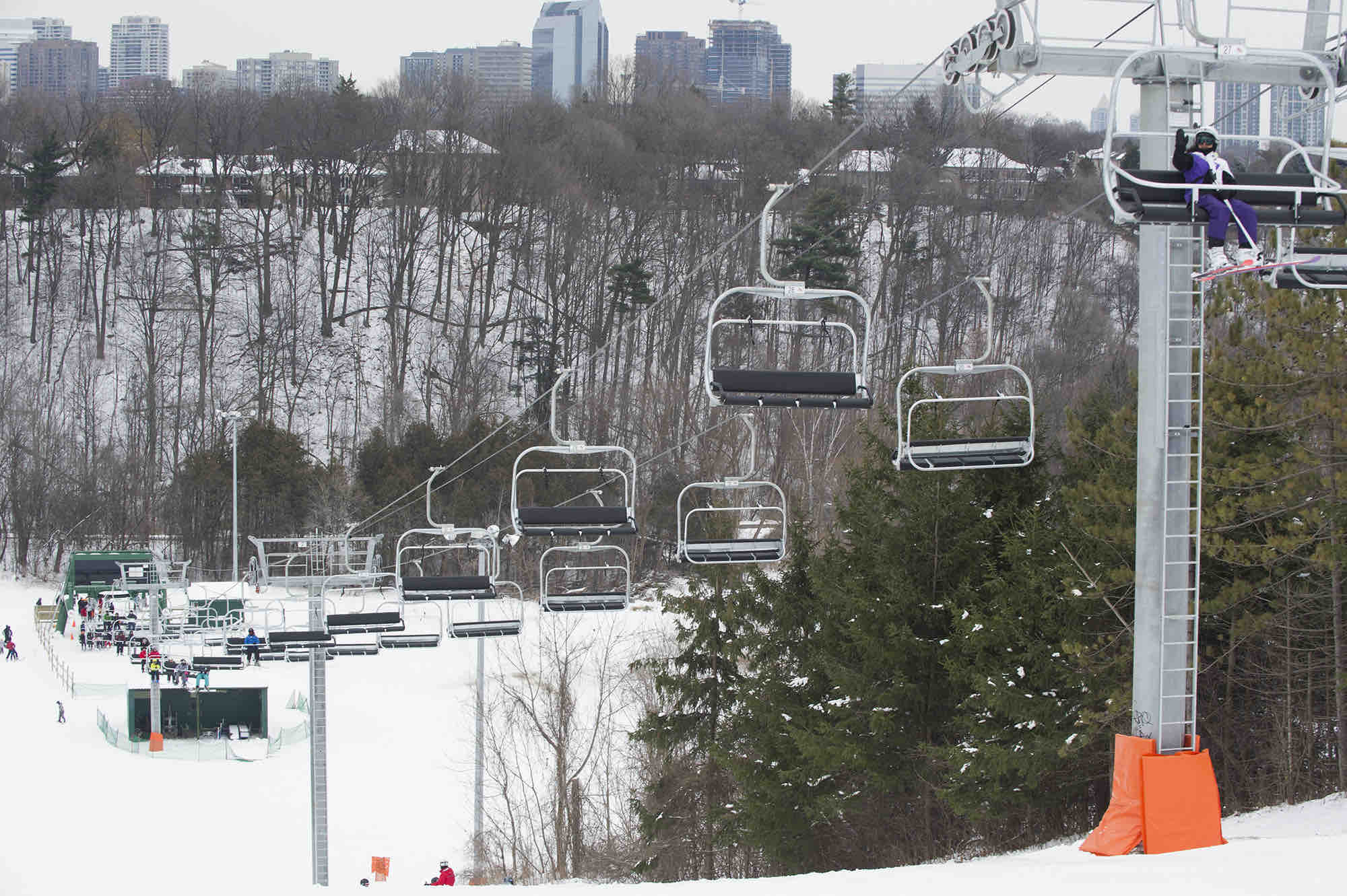 A winter scene at Earl Bales North York featuring a ski lift ascending a snowy slope bustling with skiers. The ski resort radiates a charming ambiance amidst the lovely winter scenery.