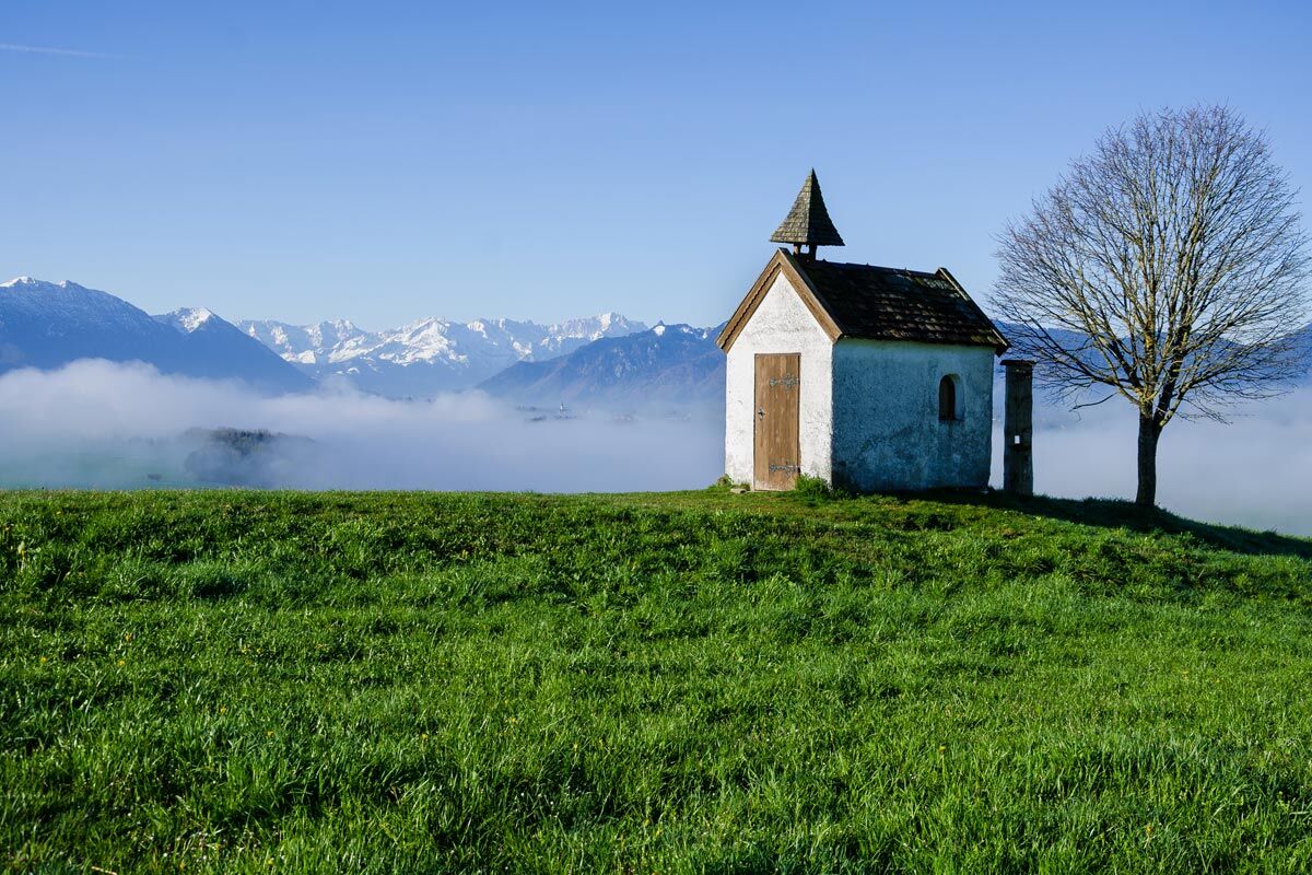 Rabenkopf – Oberau in Germany - a small house in the middle of a field with mountains in the background.